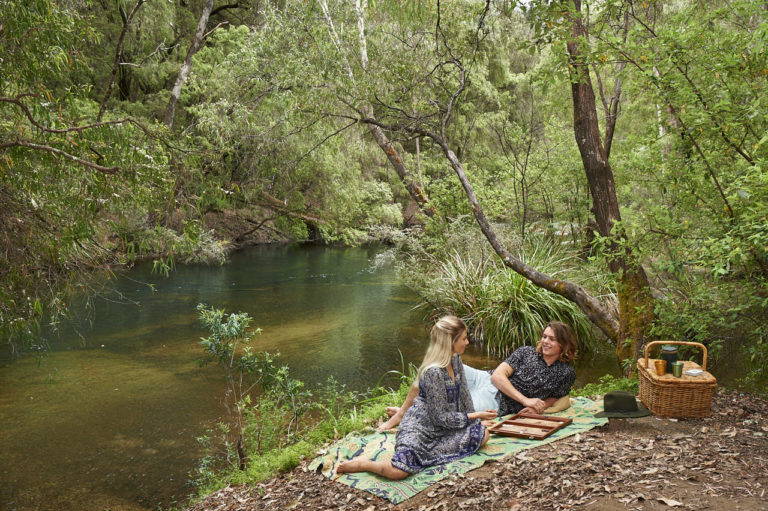 A landscape image of a couple enjoying a picnic by a green pool to show camping spots along The South West Edge road trip