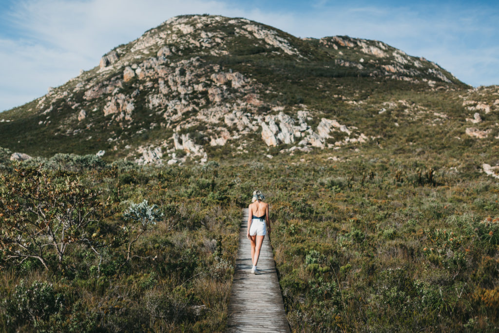 A woman walks on a boardwalk surrounded by bushland and hills