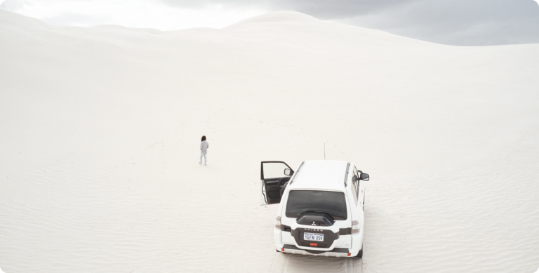 A drone image of a person walking on white sand dunes next to a four wheel drive vehicle