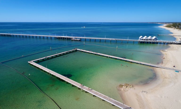 An aerial shot showing blue green ocean with a protected swimming pen and Busselton Jetty to show tourist attractions on The South West Edge road trip