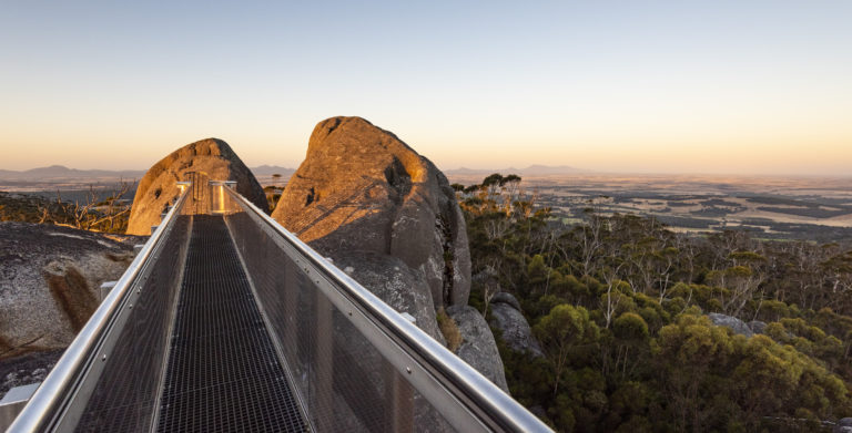 A landscape image of a metal viewing platform on top of huge boulders with sunrise view of trees and valleys to show vast landscapes on the South West Edge road trip
