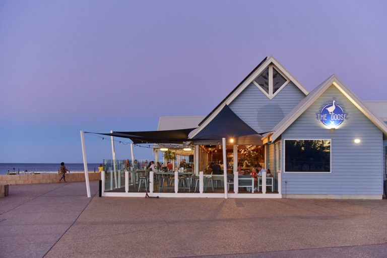 A landscape image of a cafe restaurant on the beachfront with purple sunset sky to show gourmet dining experiences on offer while driving The South West Edge road trip