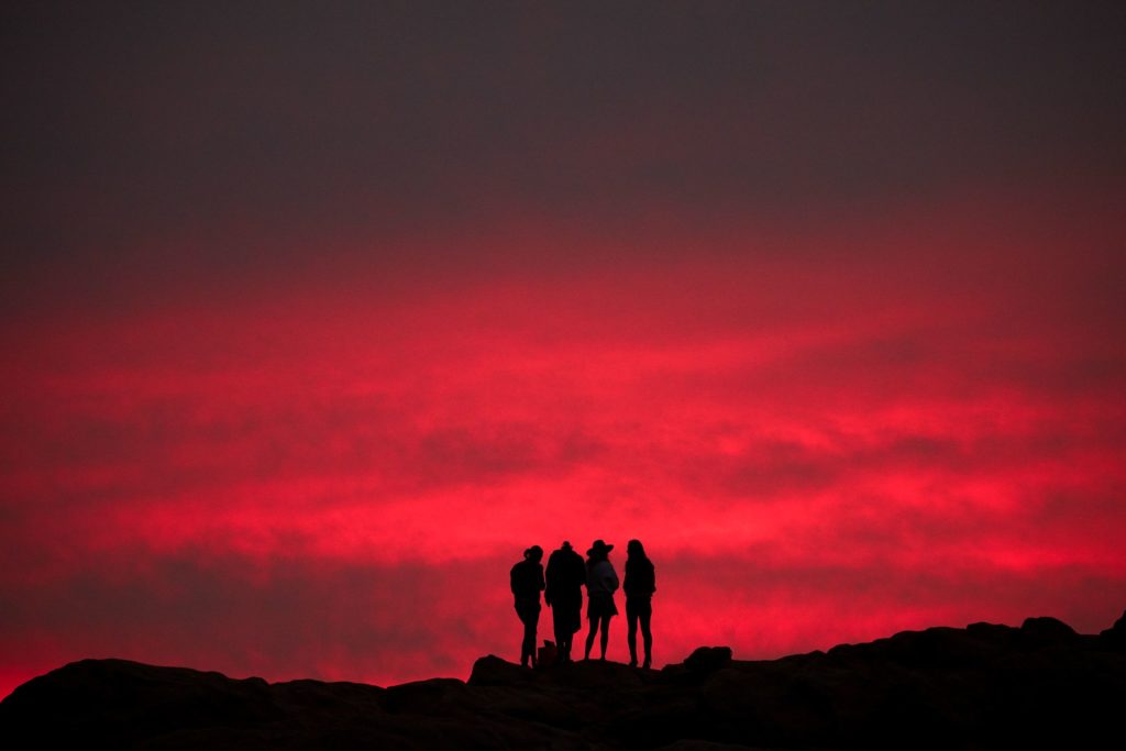 Silhouttes of four people against a deep pink cloudy sunset sky shows natural beauty found along The South West Edge road trip of south western australia