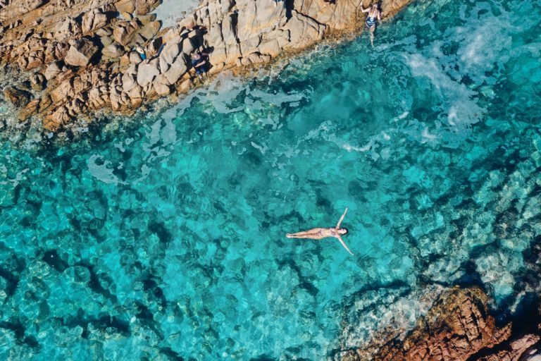 A drone image shows a woman floating in a pristine crystal clear rock pool to show natural attractions en route along The Edge road trip