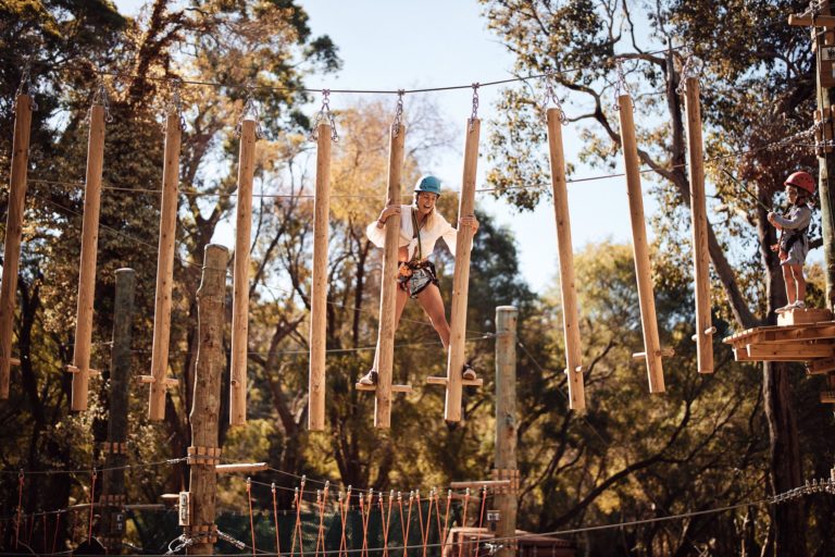 A woman laughs while doing a high ropes course in the treetops along The South West Edge to show adventurous activities to do while on this south western australia road trip