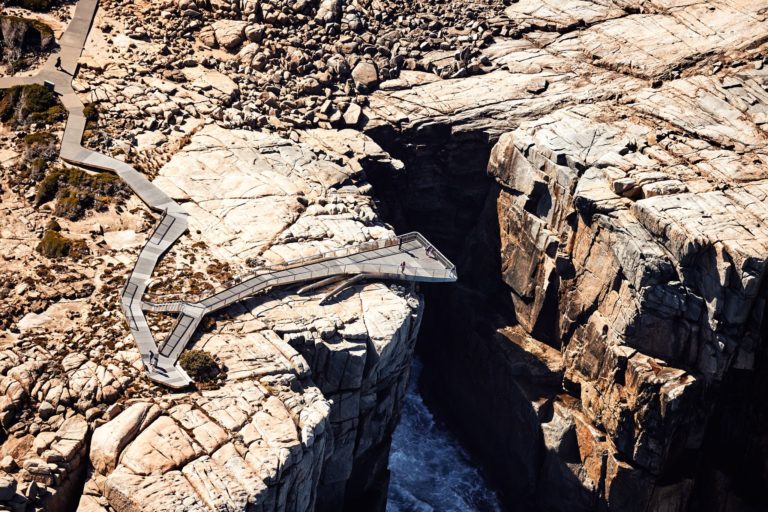 A drone image shows people standing on a disabled access viewing platform that hangs over the edge of a cliff with surging southern ocean below to show breathtaking natural attractions found on this south western australia road trip