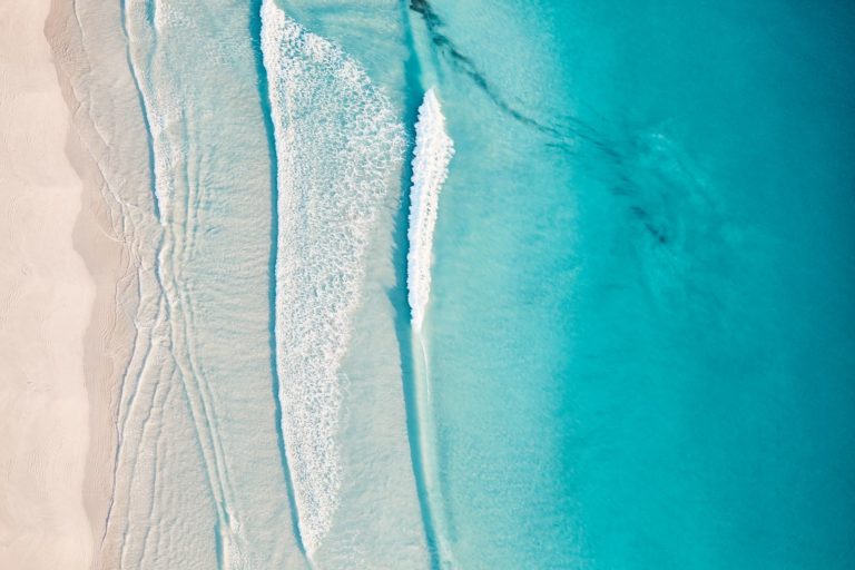 An aerial shot of pristine turquoise blue waves lapping on a white sandy beach to show untouched coastline found on the perth to esperance australia road trip