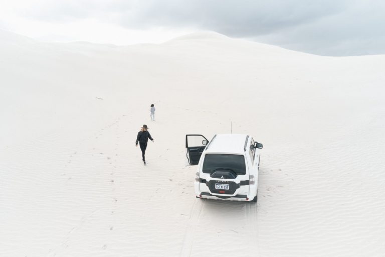 A drone image shows a four wheel drive vehicle and two people on pristine white sand dunes to show adventure in natural landscapes along The South West Edge road trip from perth to esperance