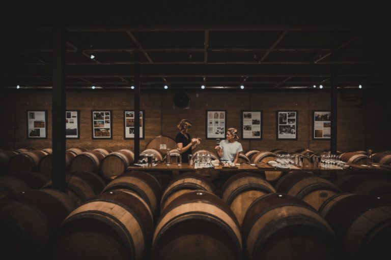 Inside a cellar door filled with wine barrels, two people enjoy a wine tasting to highlight the gourmet delights and foodie experiences to be had on The South West Edge road trip in southern western australia