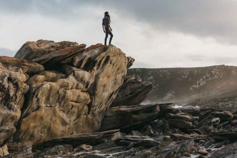 A man stands on a big rock looking at the dramatic coastline to show the rugged landscapes on the south western australia road trip perth to esperance