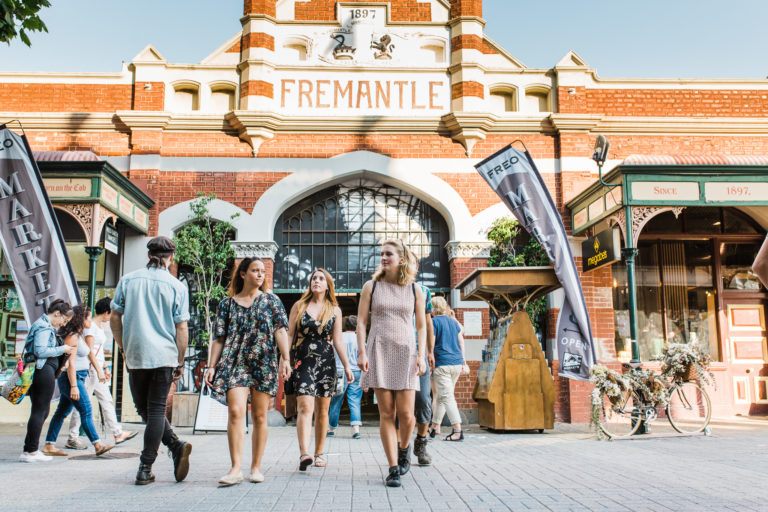 A group of young people walk outside the iconic brick Fremantle Markets building to show shopping and cultural experiences to be had on The South West Edge road trip