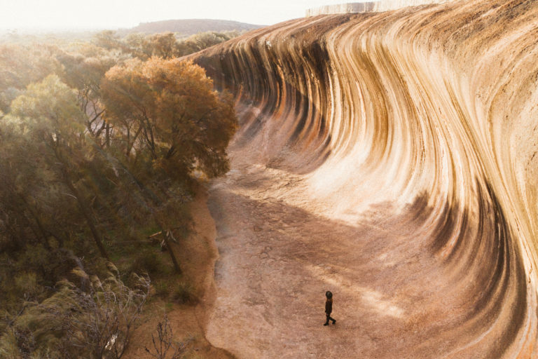 An aerial image of an impressive rock formation that resembles an ocean wave with a tiny person in the foreground shows enormous scale of impressive natural landmarks on this perth to esperance road trip