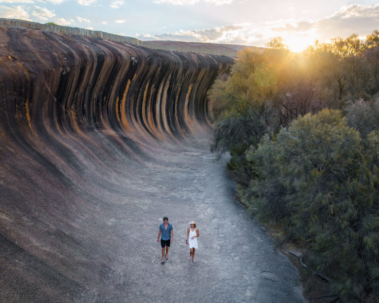 An image of a couple walking on rock face that resembles an ocean wave to show impressive natural landscapes of The South West Edge perth to esperance road trip