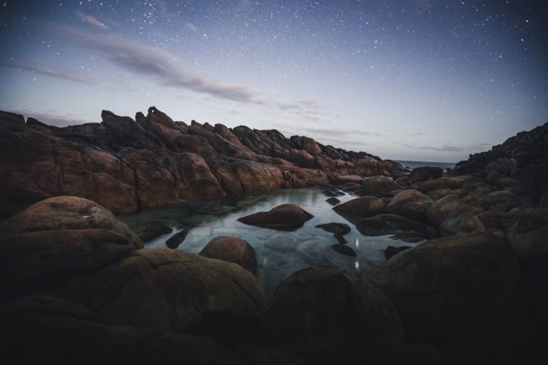 A landscape image of a quiet rock pool at dusk, with a starry night sky shows the wild beauty and natural landscapes found along The Edge road trip from perth to esperance