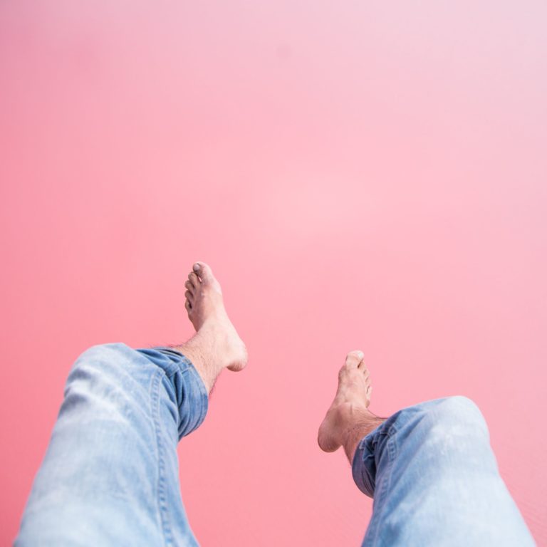 An image of legs and feet dangling over a pink salt lake shows a unique natural monument of the landscape found on the perth to esperance road trip in south western australia