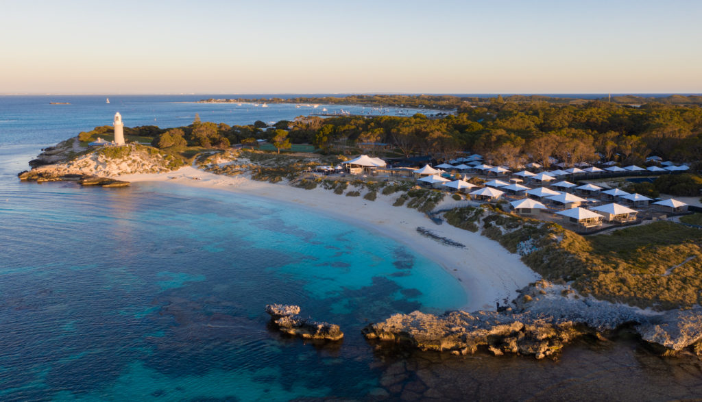 A landscape image of a calm bay with turquoise water a lighthouse and accommodation park to show attractions on Rottnest Island on The South West Edge road trip