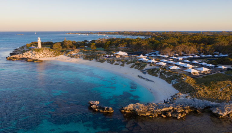 A landscape image of a calm bay with turquoise water a lighthouse and accommodation park to show attractions on Rottnest Island on The South West Edge road trip