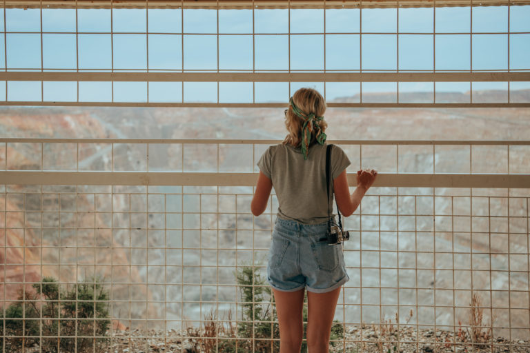 An image of a young woman at a lookout fence towards a huge open cut mine to show history and culture on The South West Edge road trip
