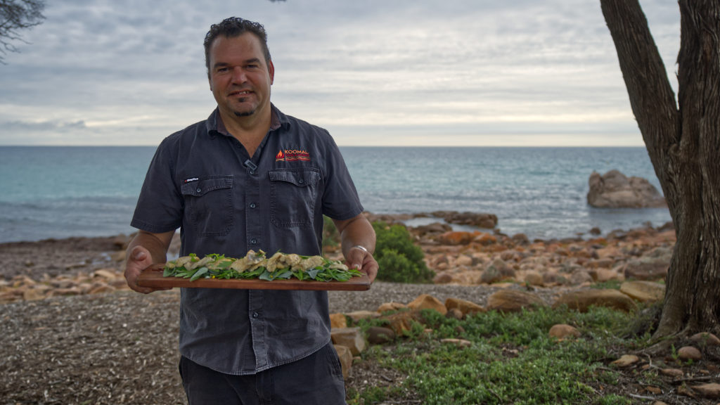 A landscape image of local Indigenous tour operator and carer of Country Josh Whiteland holding fresh native foraging to show cultural experiences en route along The Edge