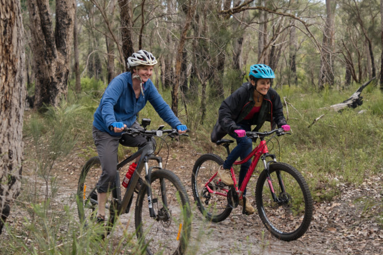 Landscape image of two ladies riding mountain bikes to show stories along the edge