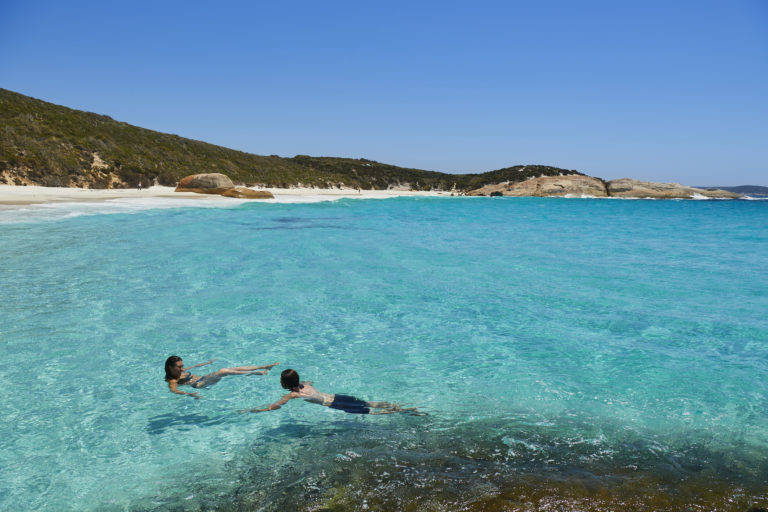 a couple swim in pristine crystal clear waters near Albany to show beaches in summer en route along The South West Edge road trip