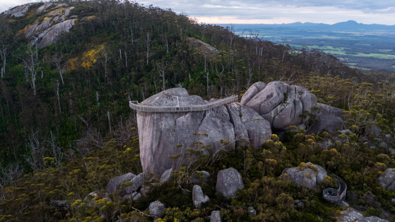 drone image of giant rock formation surrounded by vegetation and mountains to show landscapes on the south west edge