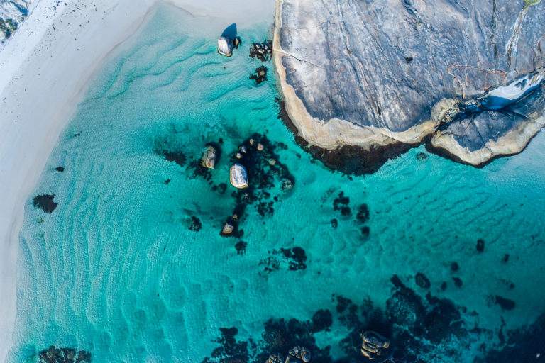 top down drone image of turquoise blue waters and boulders to show protected swimming spots en route along the edge