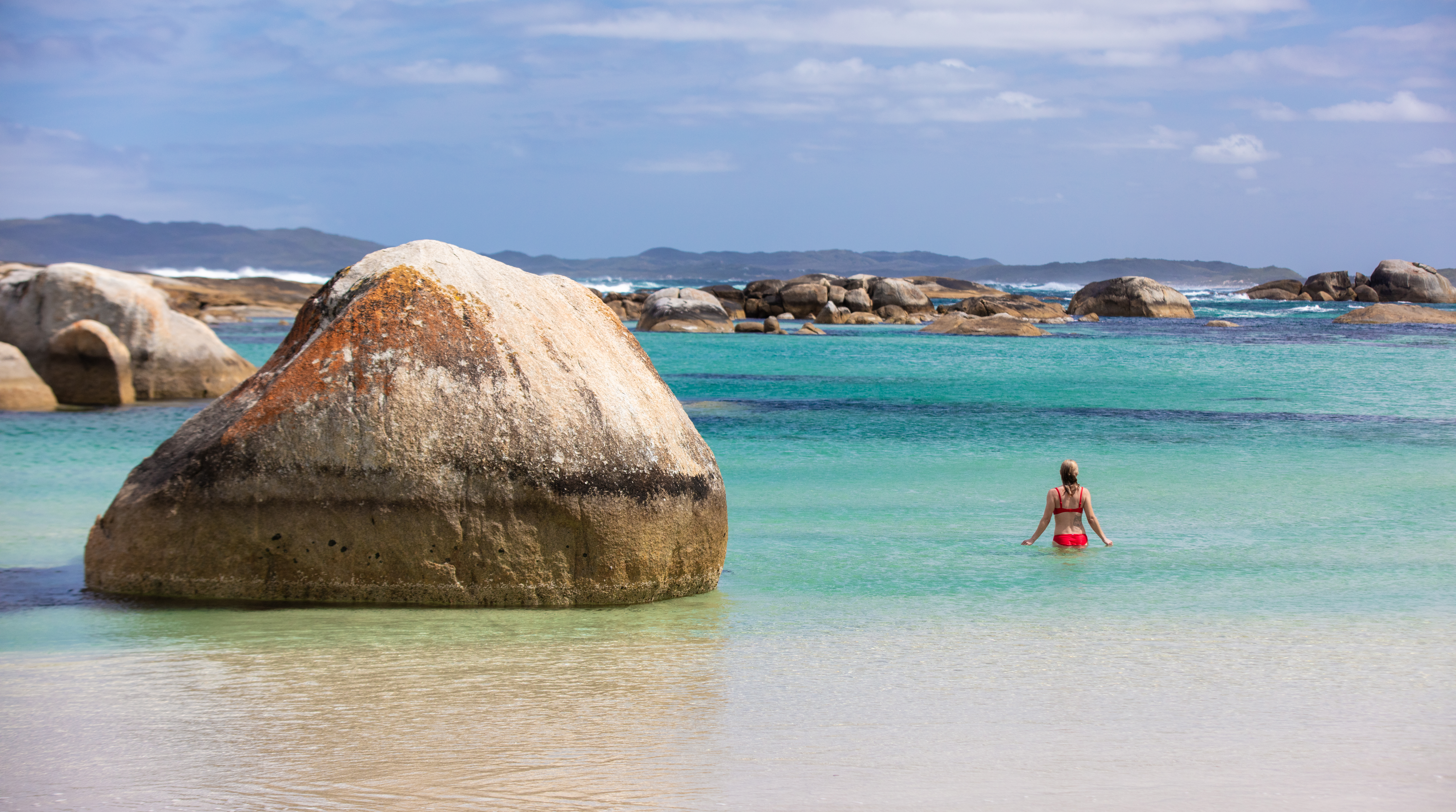 landscape image of girl in red bikini next to giant boulder in blue waters shows national parks in the south west edge are unique