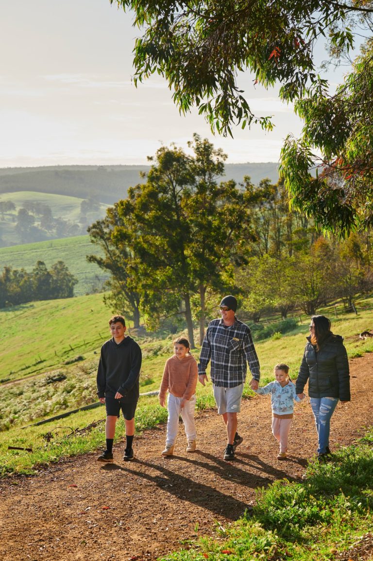 Family of five walking along a gravel path with rolling green hills and trees in the background.