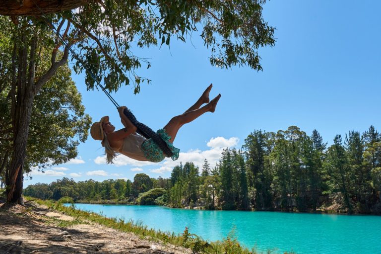 A girl swings on a tyre swing in front of turquoise blue Black Diamond Lake