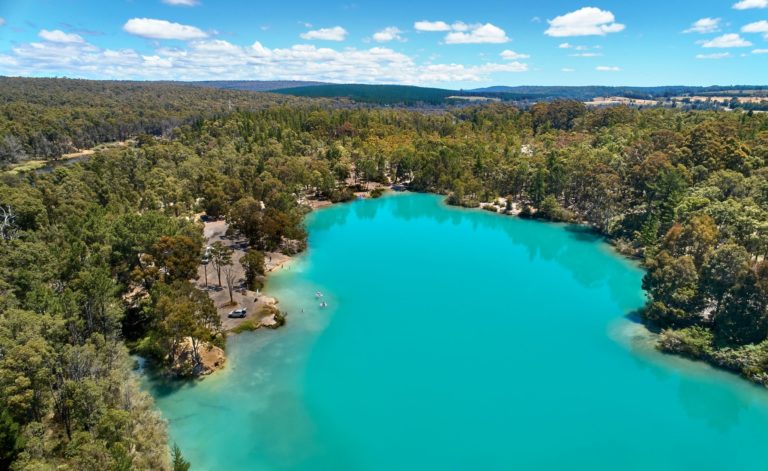 An aerial image shows a body of water that is bright turquoise blue, surrounded by green trees.