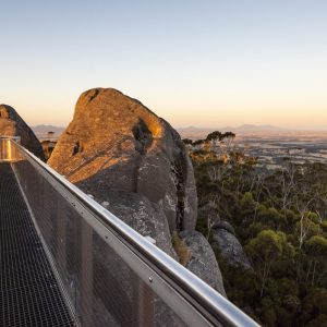 A landscape image of a metal viewing platform on top of huge boulders with sunrise view of trees and valleys to show vast landscapes on the South West Edge road trip