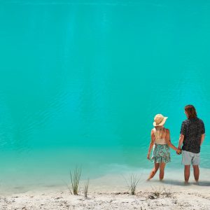 An image of a couple holding hands on the banks of a turquoise blue lake to show amazing natural attractions en route along The Edge south western australia road trip