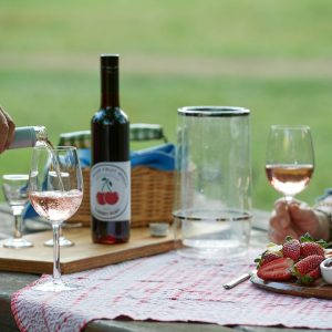 Close up image of a picnic set up on a table, with someone pouring a glass of wine next to a food platter.