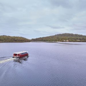 A landscape image of a small ferry putting across an inlet with trees in the distance shows nature and experiences had on The South West Edge road trip