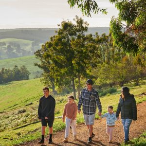 Family of five walking along a gravel path with rolling green hills and trees in the background.