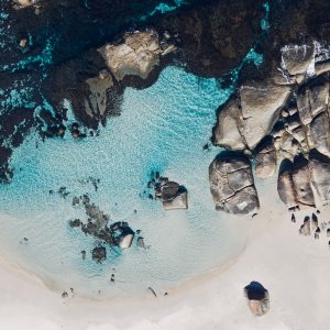 A drone image of crystal clear blue ocean on a beach with boulders to show the incredible natural attractions along The South West Edge road trip