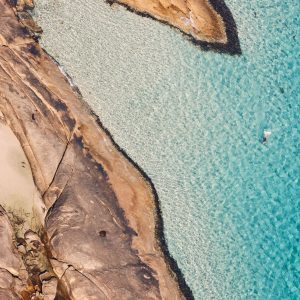 A drone image of a lone swimmer in crystal blue ocean water to show pristine natural attractions on the south western australia road trip The Edge