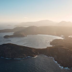 An aerial shot of rocky ocean cliffs with misty sun to show the natural beauty found on The South West Edge road trip from perth to esperance