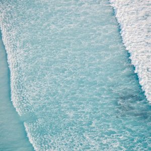 An aerial shot of lapping frothy waves of crystal blue ocean show the untouched natural beauty found on the perth to esperance road trip The Edge