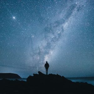 A person stands silhoutted on a rock with an amazing view of the milky way and millions of stars in the blue sky to show the secluded natural monuments found on The South West Edge road trip from perth to esperance