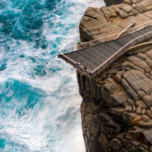 A portrait image of people looking over the edge of a viewing platform that hangs off a cliff over the southern ocean to show the rugged landscape and wild beauty found on the perth to esperance road trip The Edge