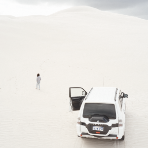 A drone image of a person walking on white sand dunes next to a four wheel drive vehicle