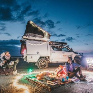 A couple has a twilight picnic on a beach with a four wheel drive suitable for camping