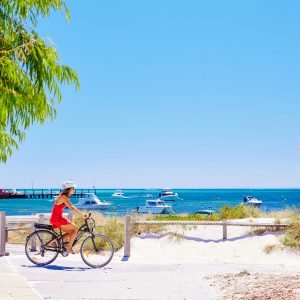 An image of a woman riding a bike with white sand and beach in the background to show outdoor attractions on The South West Edge road trip