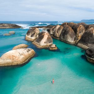 drone image of girl in peppermint coloured waters with giant boulders to show epic beaches on The South West Edge road trip